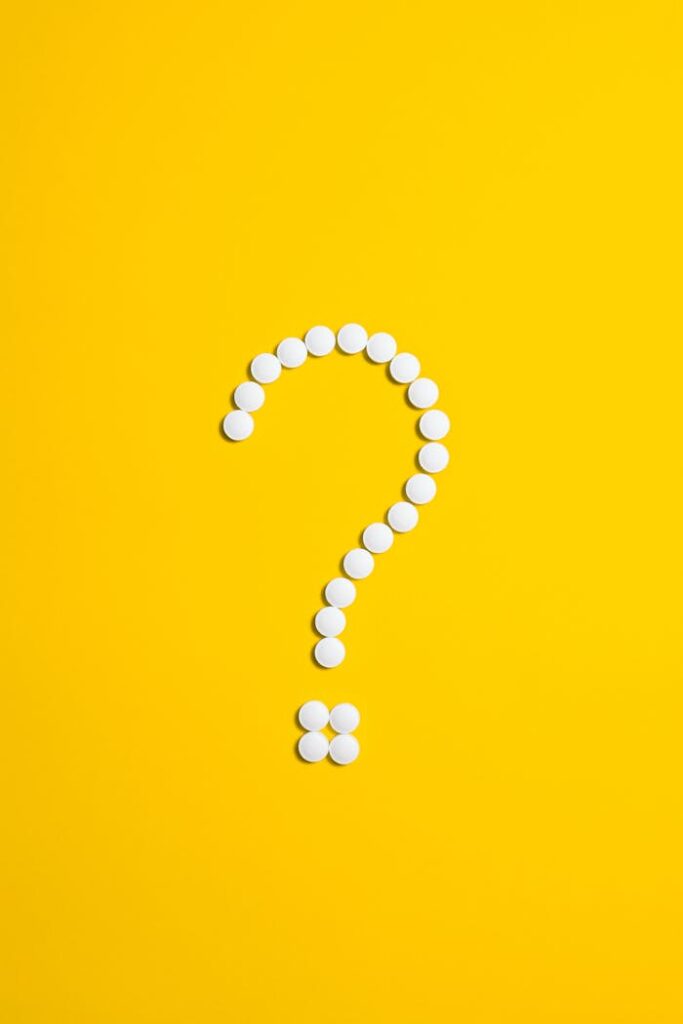White pills arranged in a question mark shape on a bright yellow background, symbolizing medical queries.